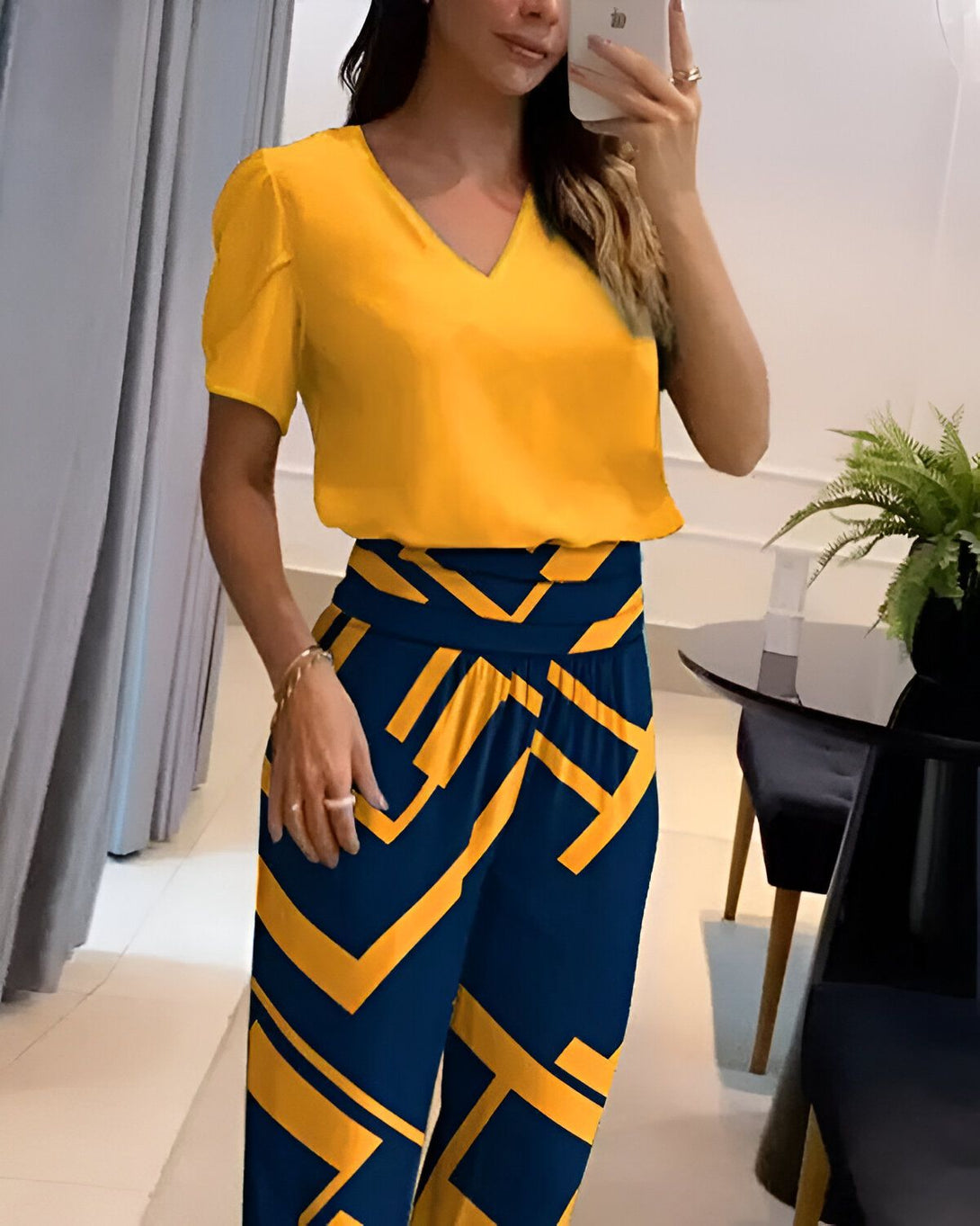 Une femme porte un chemisier jaune à manches courtes et un pantalon bleu marine à motifs géométriques jaunes.