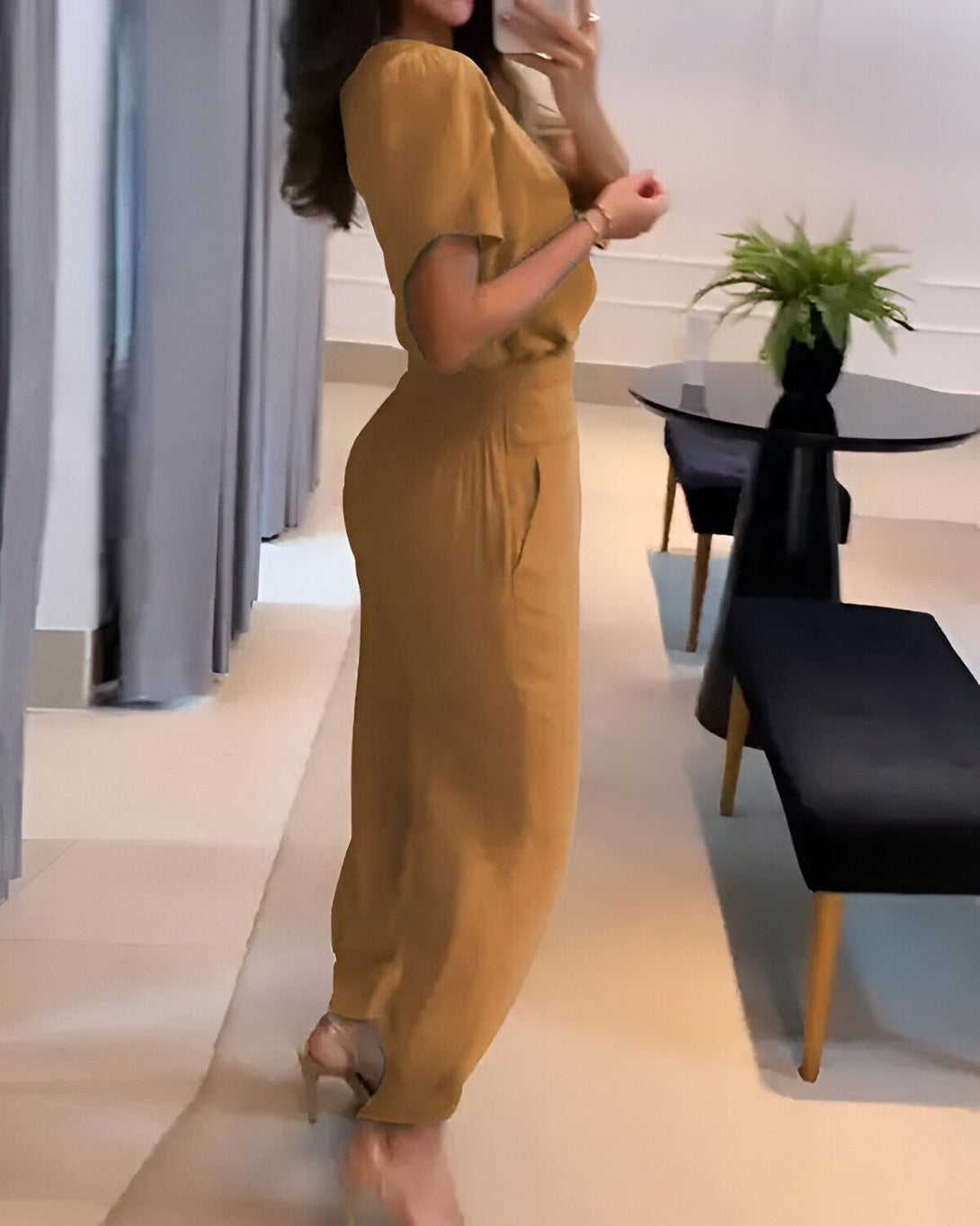 Une femme portant un tailleur pantalon marron composé d'un chemisier à manches courtes et d'un pantalon taille haute. Elle est vue de dos et porte des sandales à talons hauts.