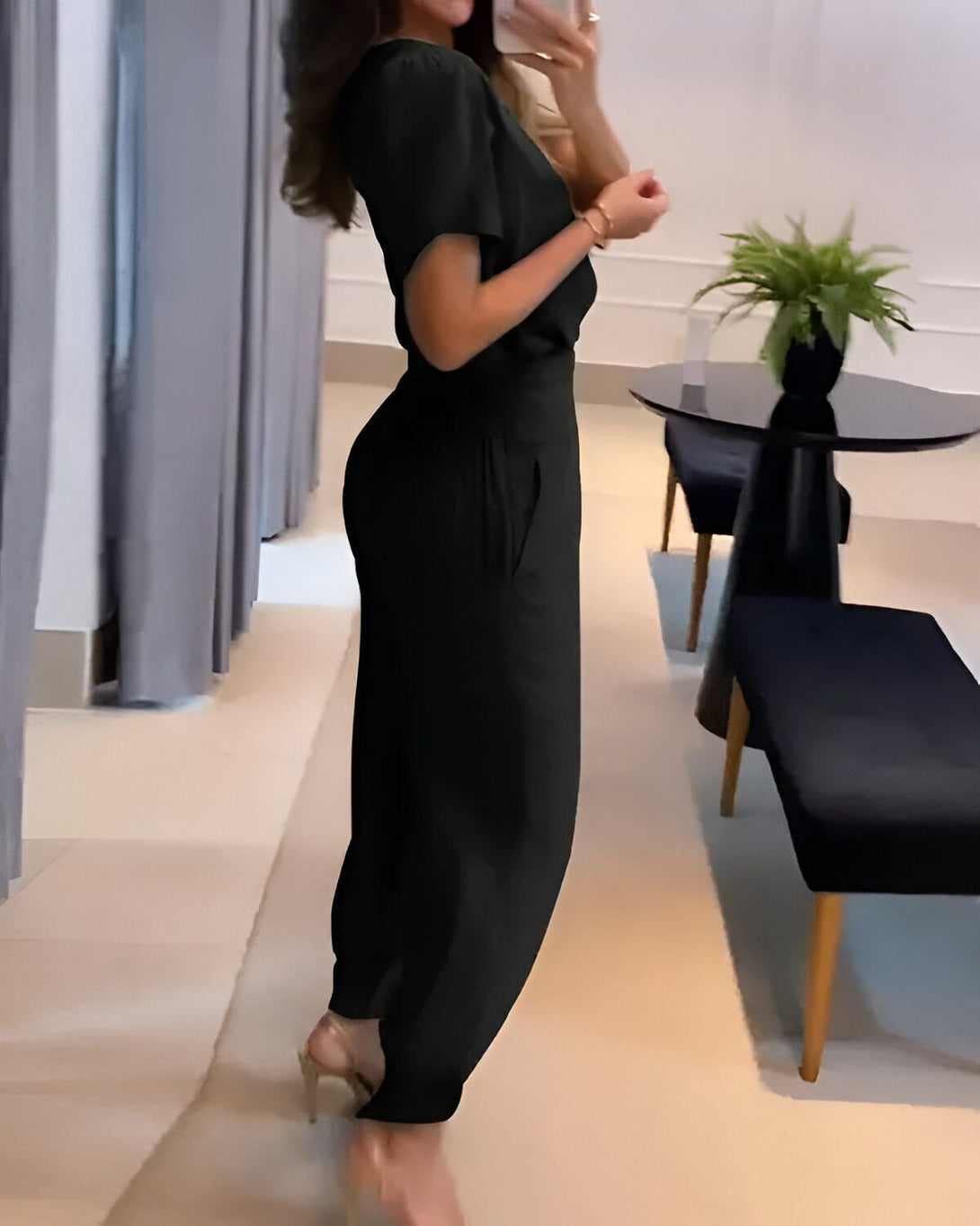 Une femme portant un tailleur pantalon noir. Elle est vue de dos et porte des sandales à talons hauts.