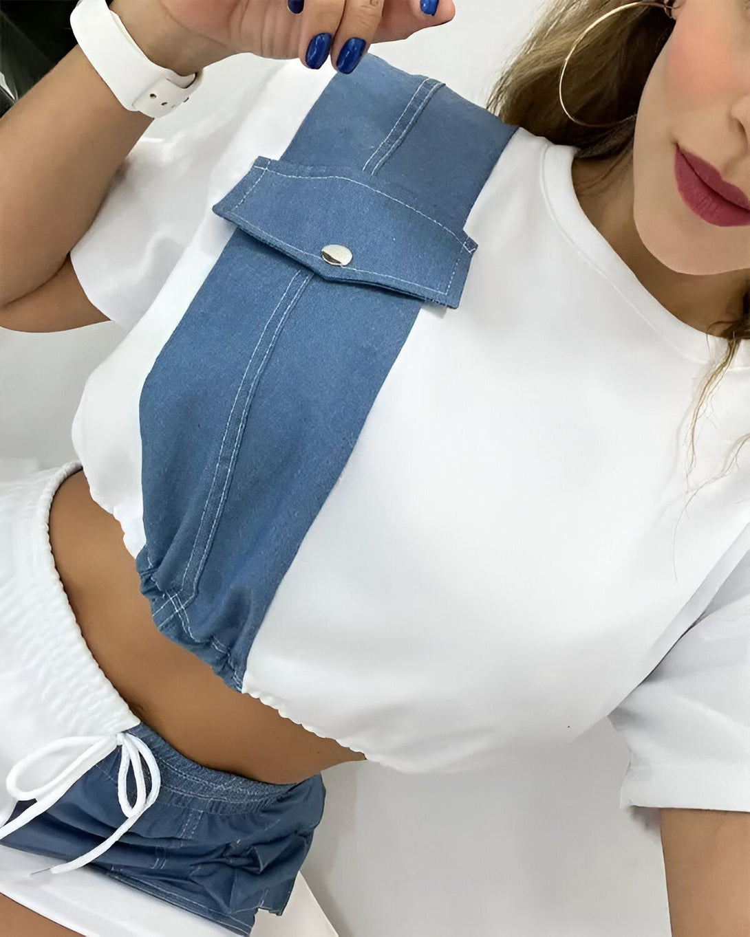 Une jeune femme porte un crop top blanc et bleu avec une poche sur le devant. Elle porte également un short bleu assorti.