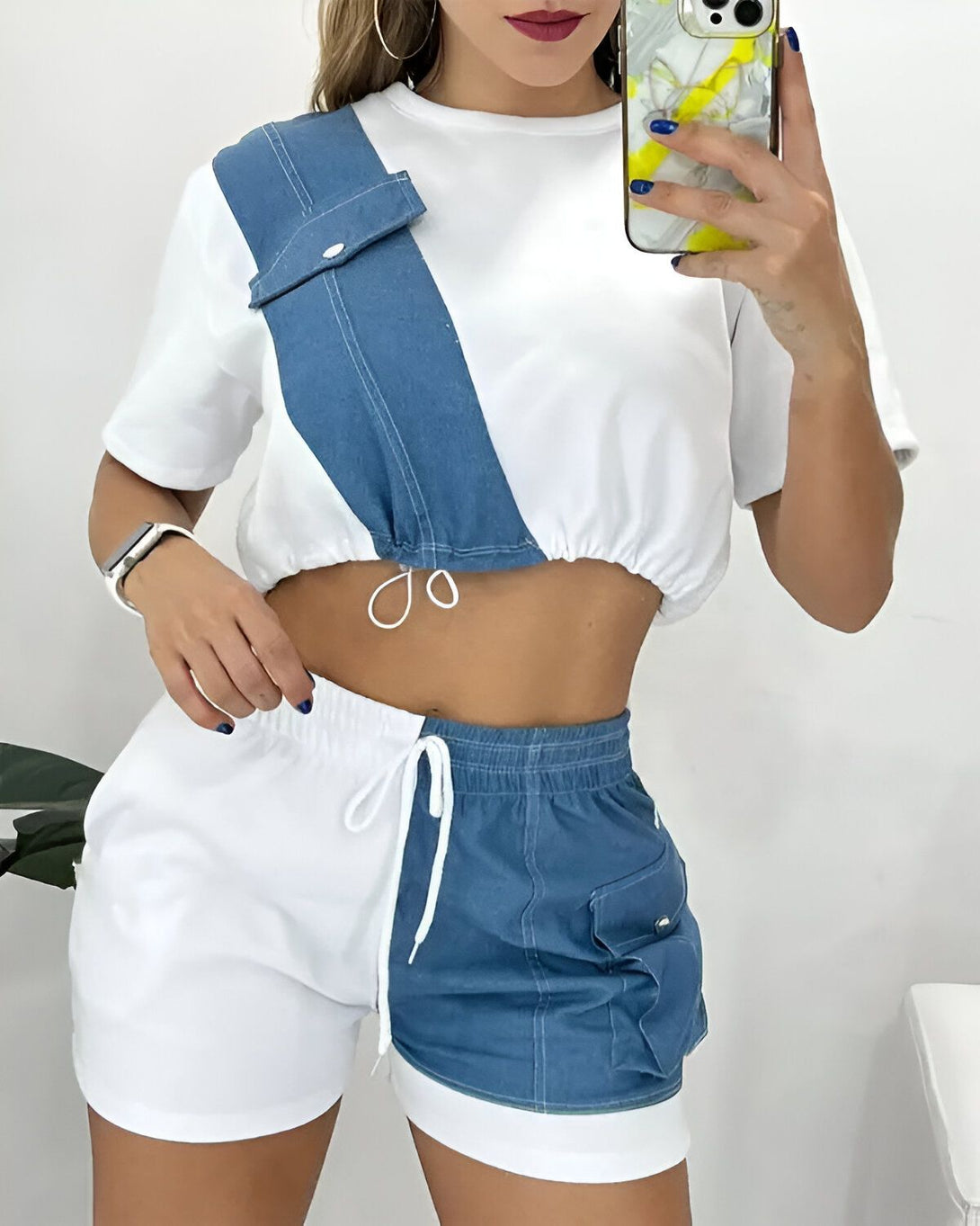 Une femme porte un ensemble short et haut de couleur bleu et blanc. Le haut est court et possède une poche sur le devant. Le short est taille haute et possède des poches sur les côtés.
