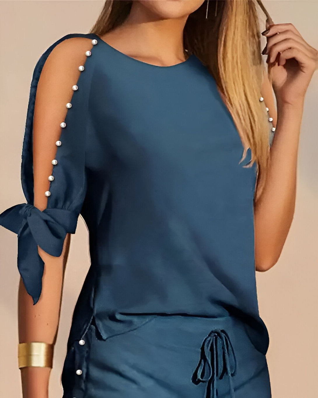 Une femme porte un chemisier bleu marine à manches courtes avec des perles sur les épaules et un pantalon bleu marine assorti.