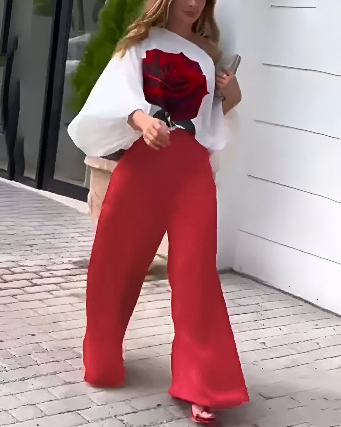 Une femme porte un pantalon rouge et un chemisier blanc avec une image de rose rouge.