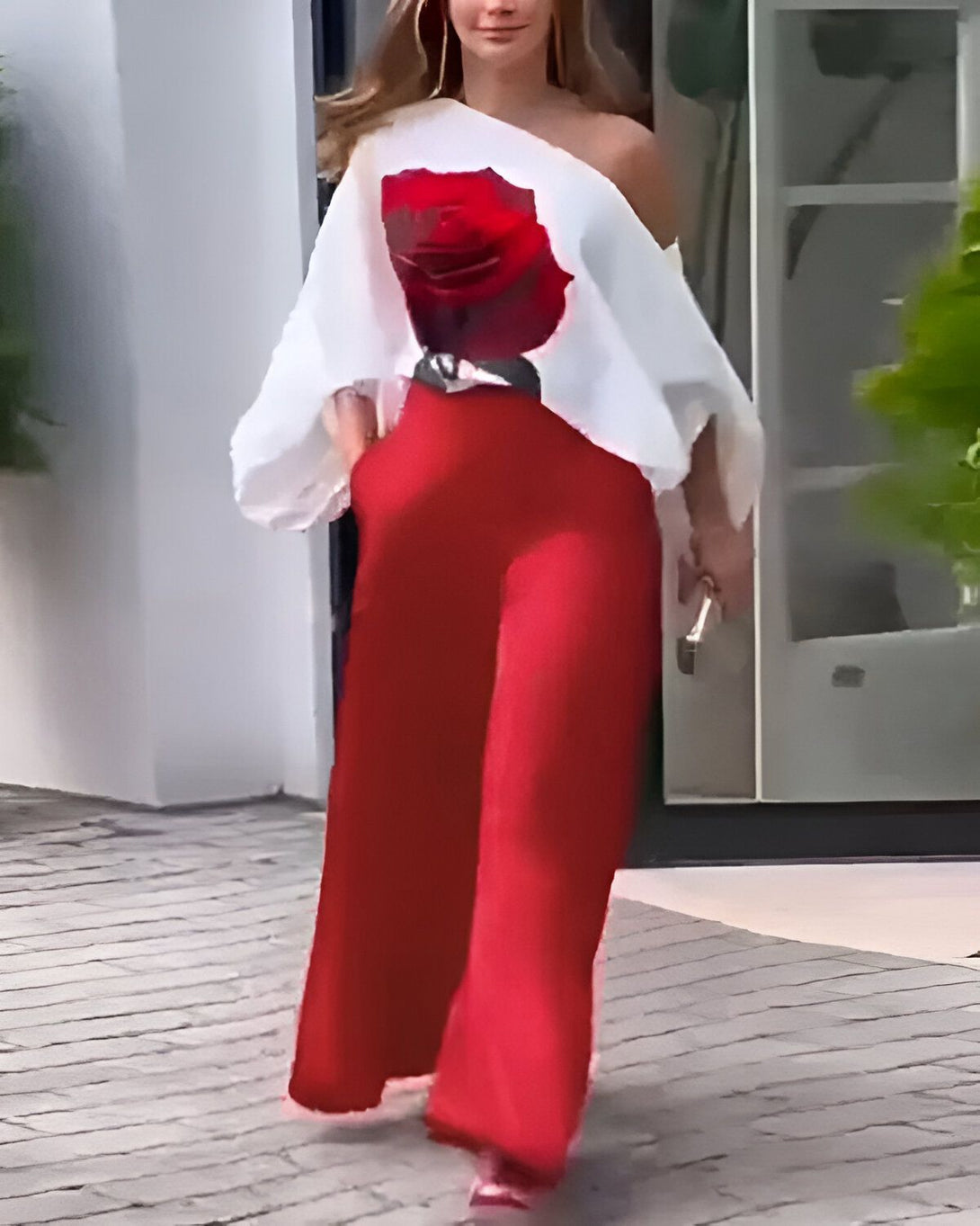 Une femme porte un pantalon rouge et un chemisier blanc à épaules dénudées avec une rose rouge imprimée sur le devant.