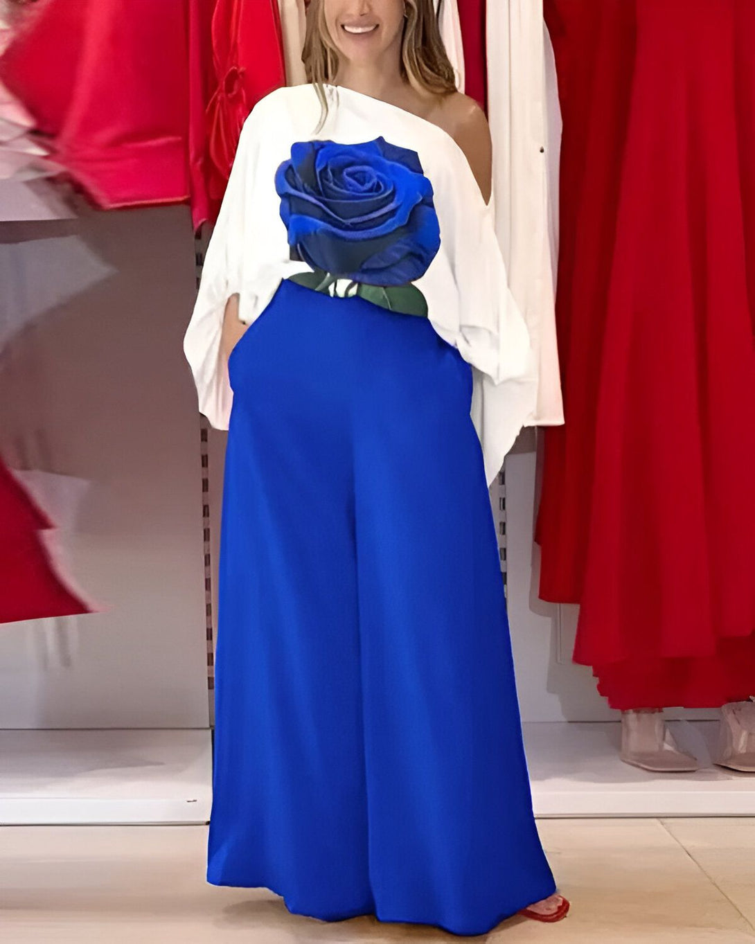 Une femme porte un chemisier blanc avec une rose bleue imprimée sur le devant et un pantalon bleu assorti.