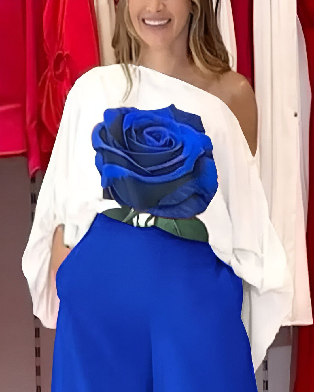 Une femme porte un chemisier blanc avec une image d'une rose bleue imprimée dessus. Elle porte également un pantalon bleu et sourit à la caméra.