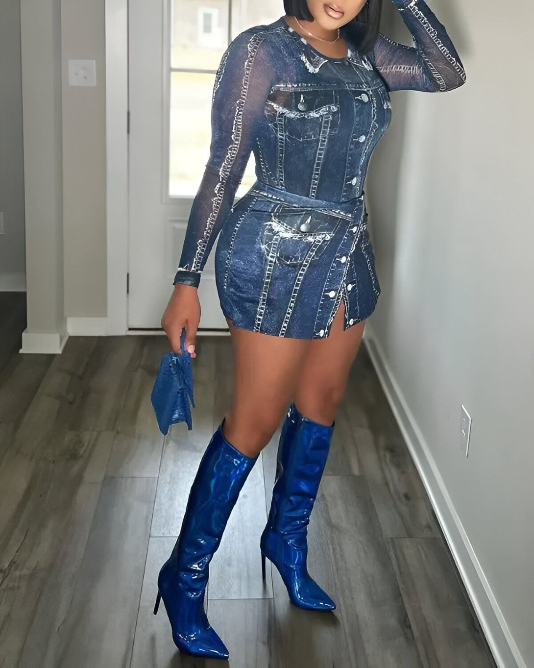 Une femme porte une robe en jean bleu et des bottes bleues. Elle est debout dans une pièce avec un sol en bois et une porte blanche.