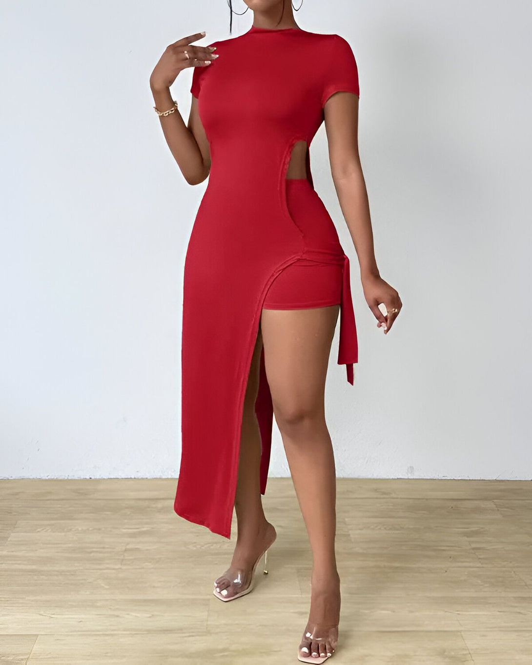 Une femme porte une robe rouge moulante avec une fente sur le côté. Elle porte également des talons transparents.