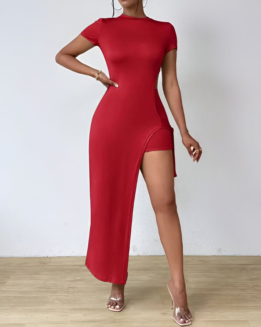 Une femme porte une robe rouge moulante fendue sur le côté. Elle porte également des sandales à talons transparentes.