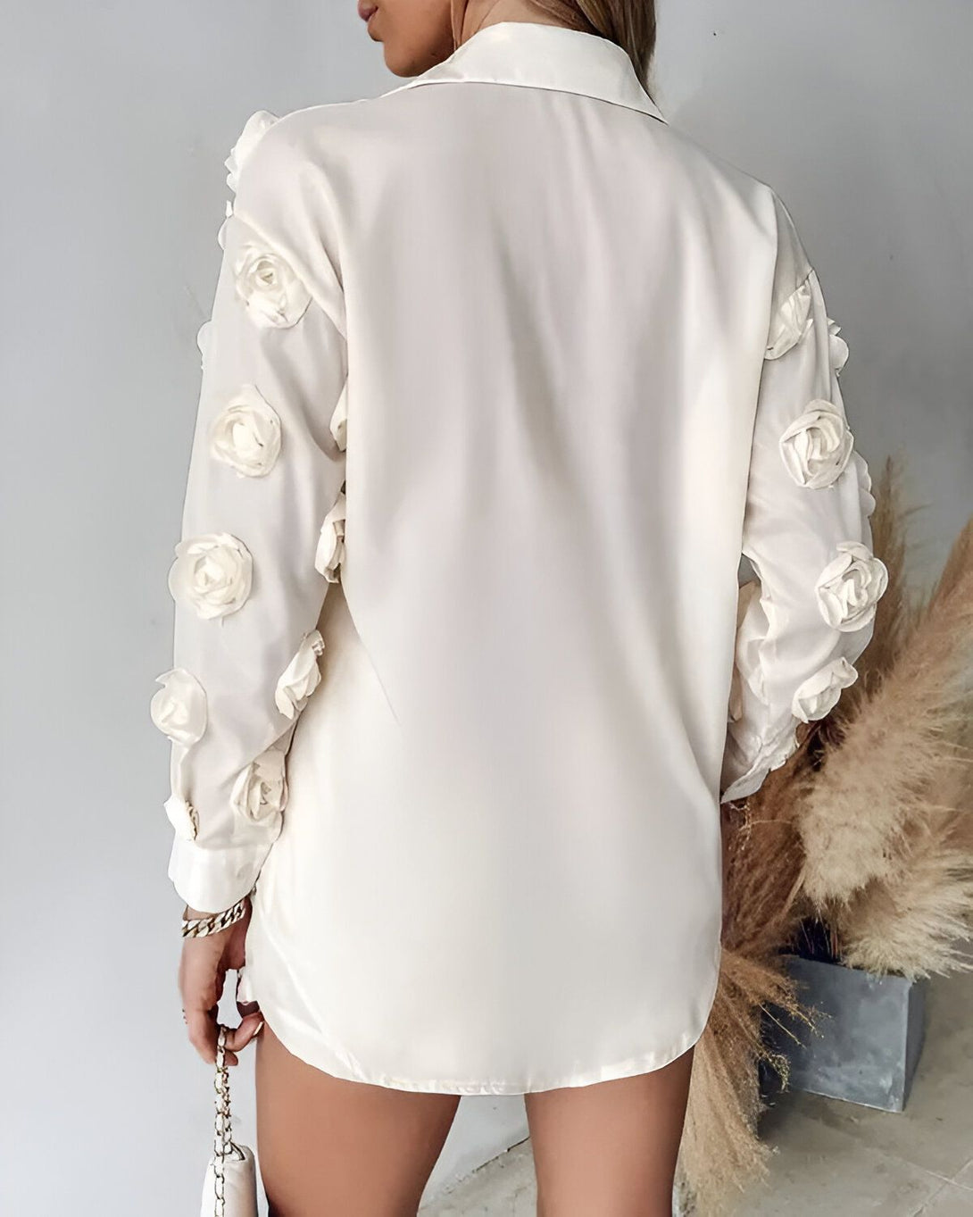 Une femme porte une chemise blanche avec des manches bouffantes décorées de roses en tissu.