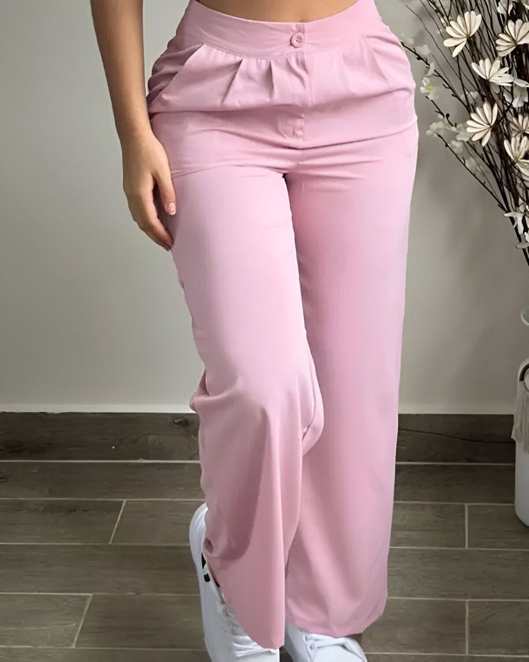 Une femme porte un pantalon rose ample et taille haute. Elle est vue de face et porte des baskets blanches. Le pantalon est en tissu léger et fluide.