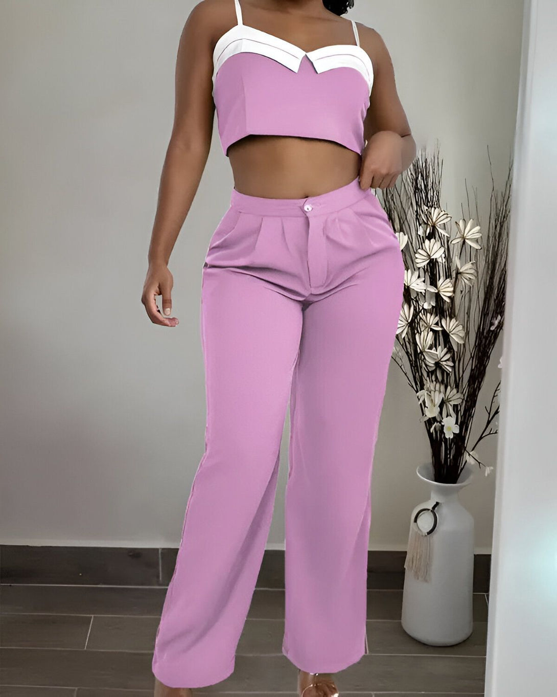 Une femme porte un ensemble pantalon et haut de couleur rose. Le haut est court et le pantalon est large.