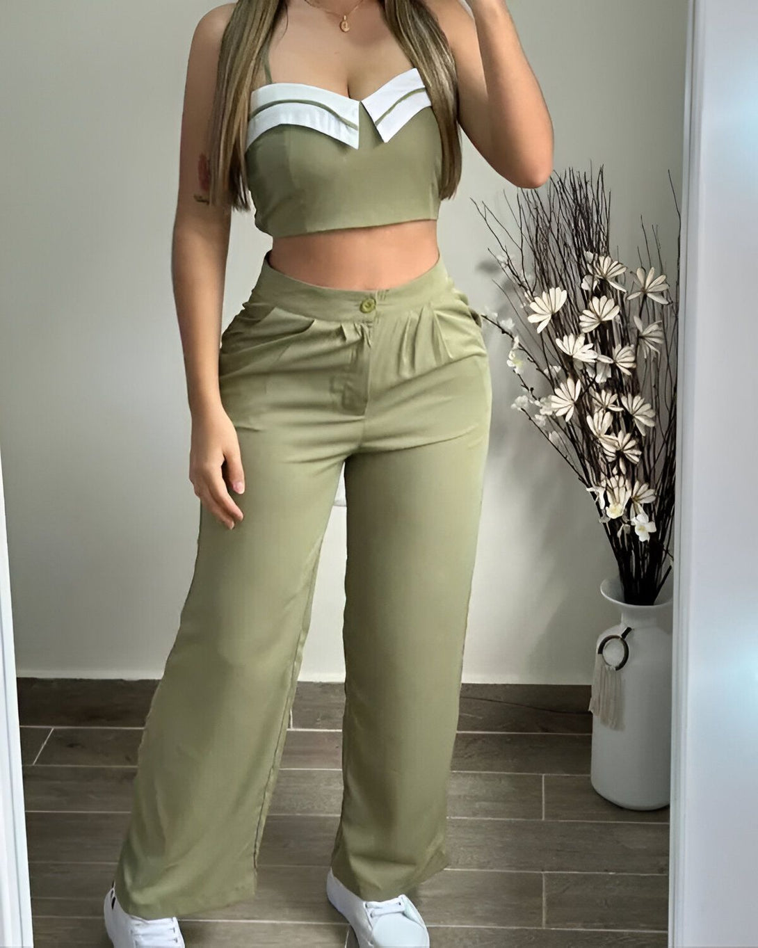 Une femme porte un ensemble pantalon et haut vert kaki. Le haut est court et possède un col blanc. Le pantalon est large et taille haute.