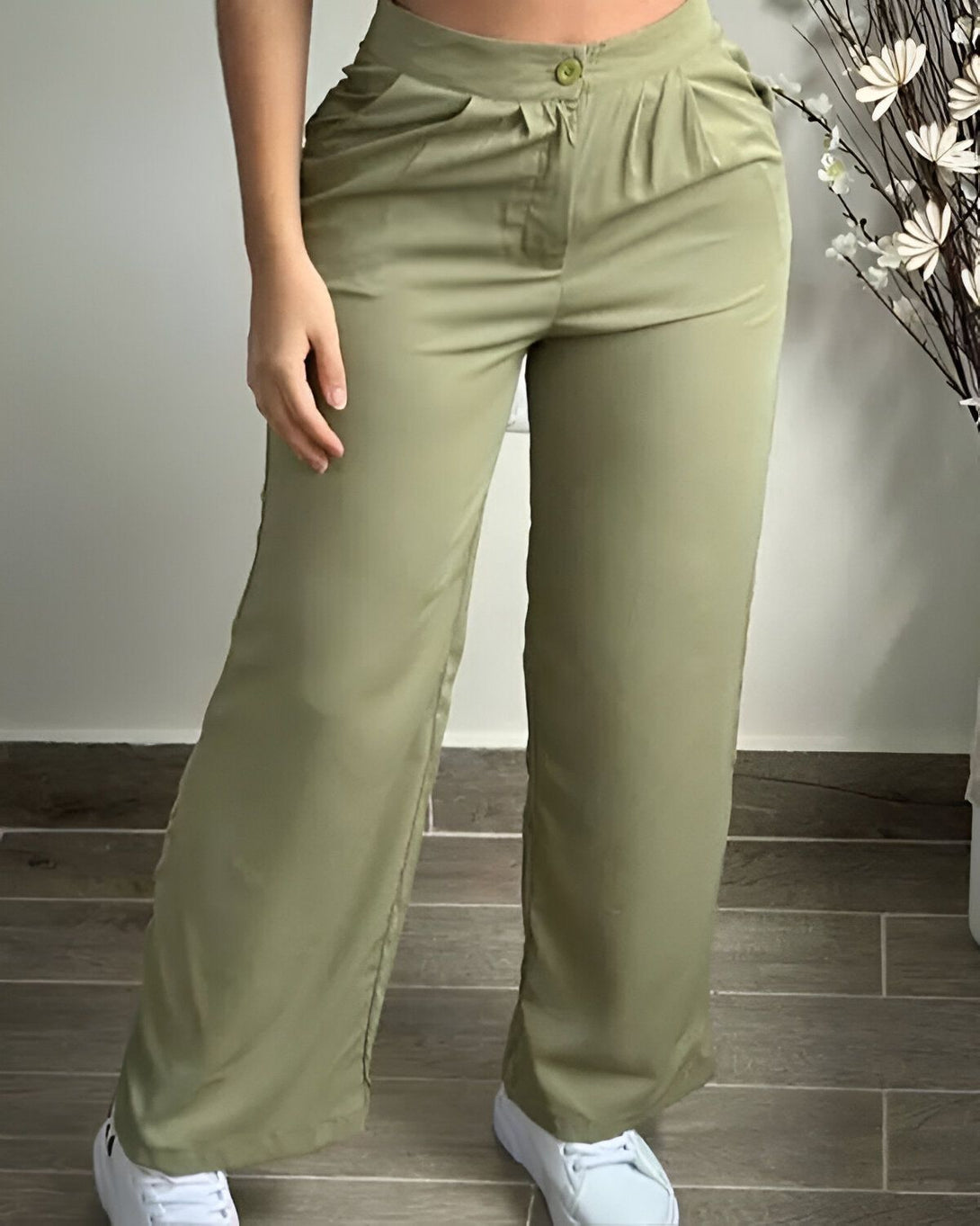 Une femme porte un pantalon large vert olive taille haute avec une ceinture à bouton. Elle est également porte des baskets blanches et un haut blanc.