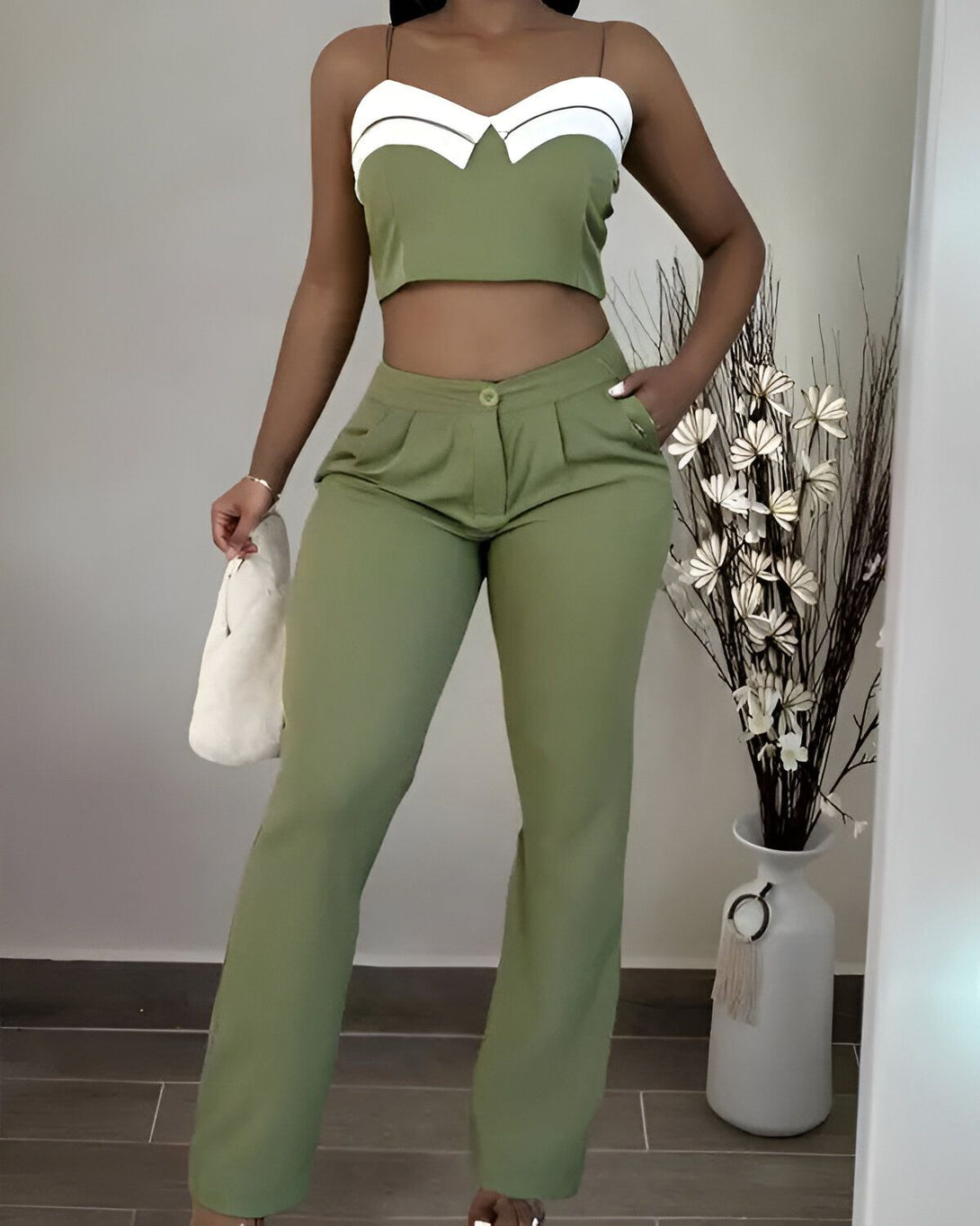 Une femme porte un ensemble pantalon et haut vert. Le haut est court et possède un décolleté en V. Le pantalon est taille haute et évasé. La femme porte également un sac à main blanc.