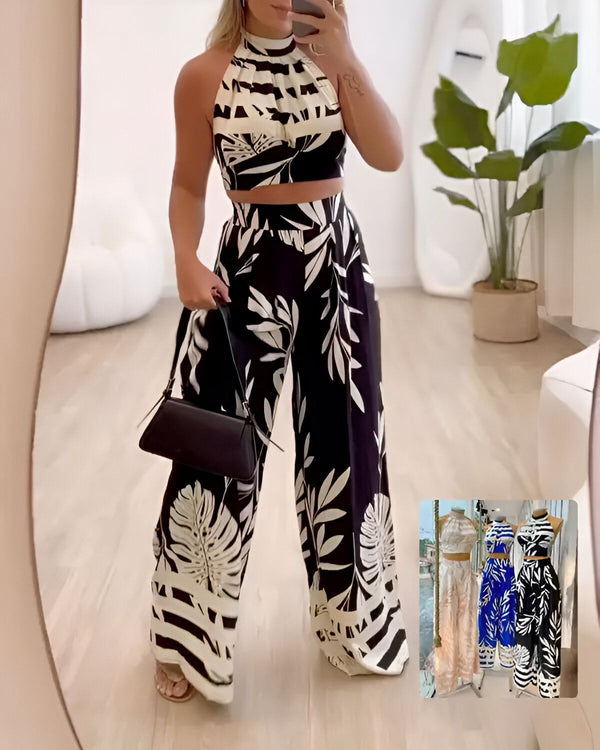 Une femme porte un haut court noir et blanc et un pantalon large noir et blanc. Le haut est court et a un col montant. Le pantalon est ample et a une taille haute. La femme porte également un sac à main noir et des sandales noires.