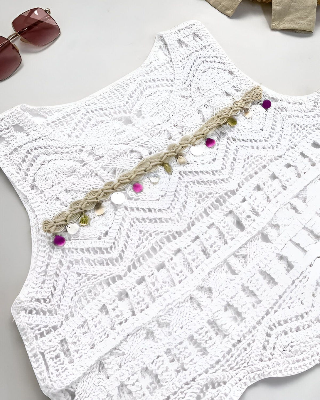 Une image d'un gilet en dentelle blanc avec des perles colorées.