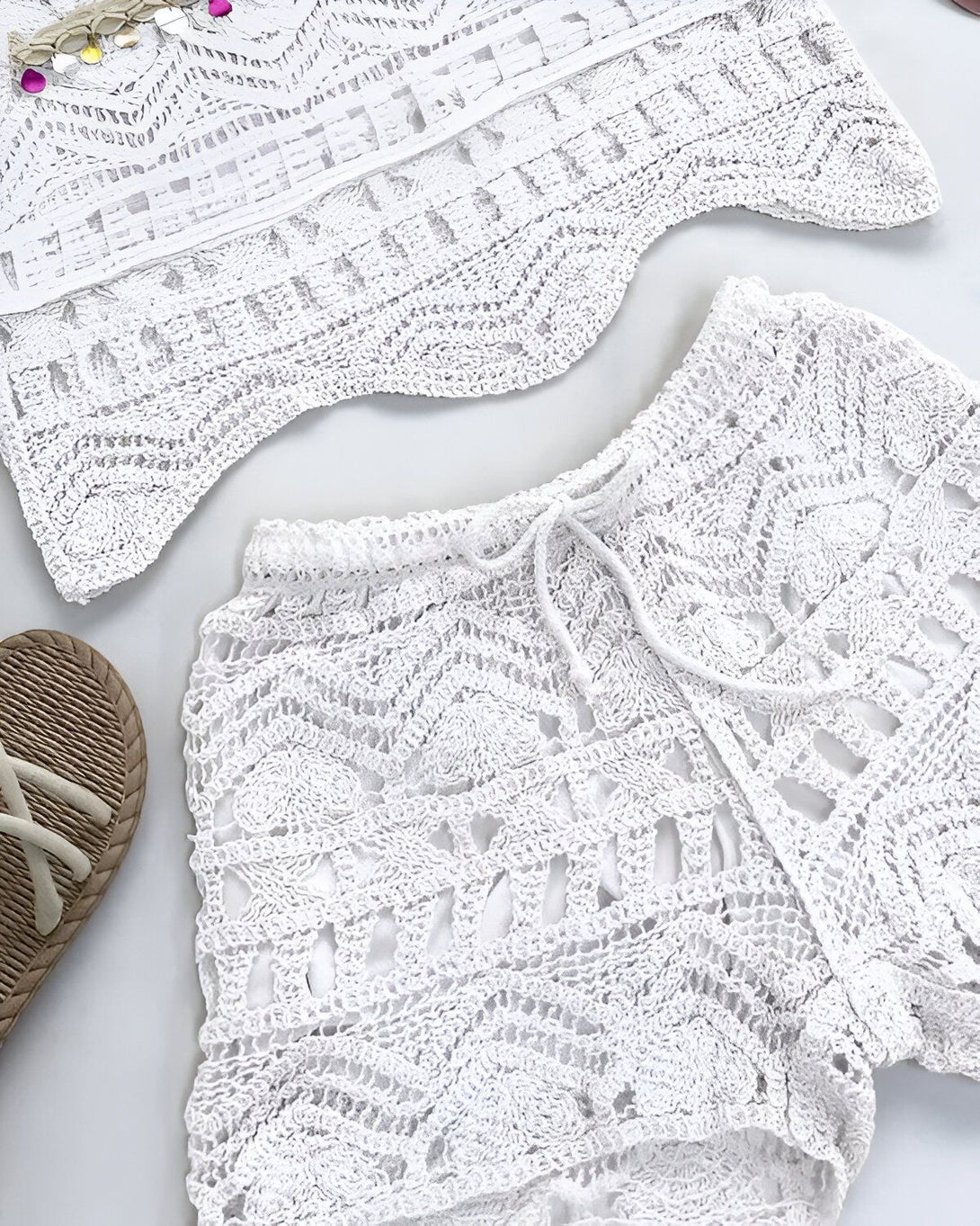 Une image d'un short et d'un haut en crochet blanc. Le short est taille haute et possède une ceinture à nouer. Le haut est court et possède des manches courtes. Les deux pièces sont en crochet avec un motif ajouré.