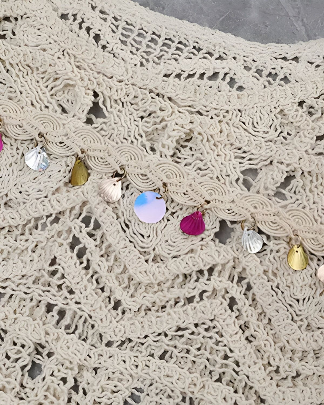 Une image d'un vêtement de plage en crochet beige avec des coquillages et des sequins argentés, dorés et roses.