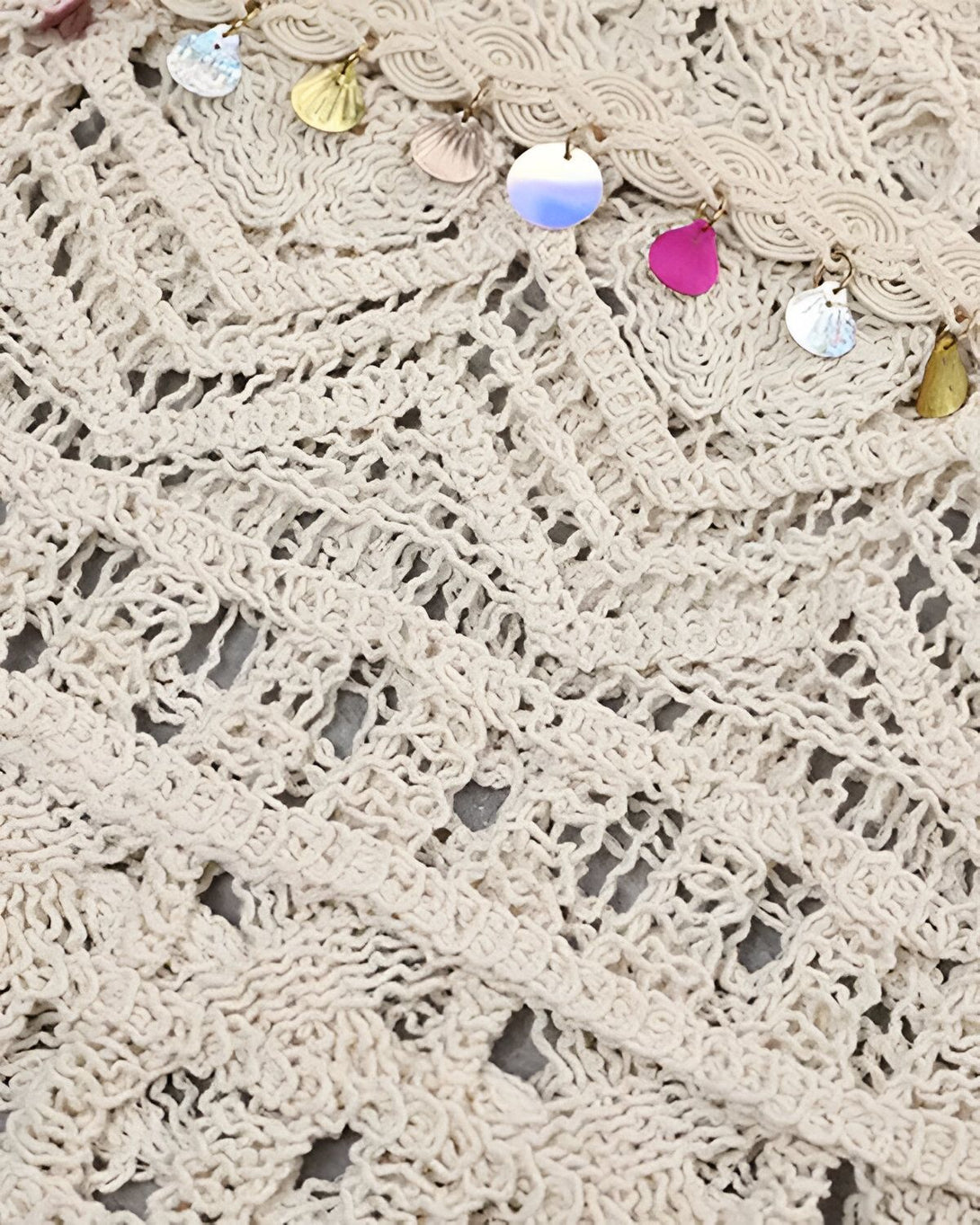 Une image de près d'un vêtement en crochet beige avec des coquillages et des perles colorées.