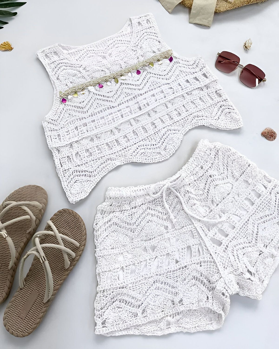 Une image d'un haut et d'un short en crochet blanc. Le haut est court et sans manches, avec un col en V. Le short est taille haute et a une coupe ample. Les deux pièces sont faites d'un fil de coton fin et léger.