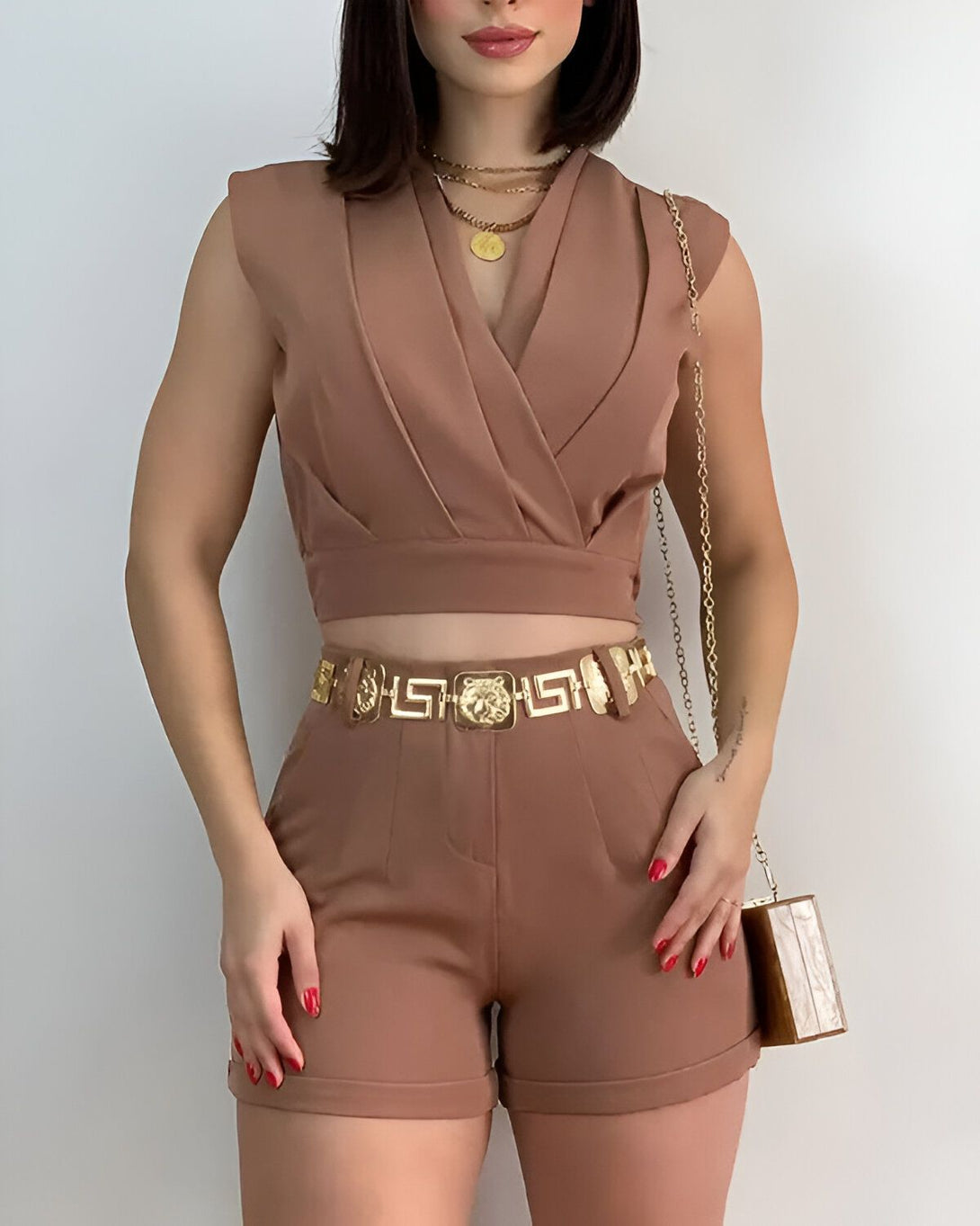 Une femme porte un ensemble marron composé d'un crop top et d'un short taille haute. Elle porte également une ceinture dorée et un collier.