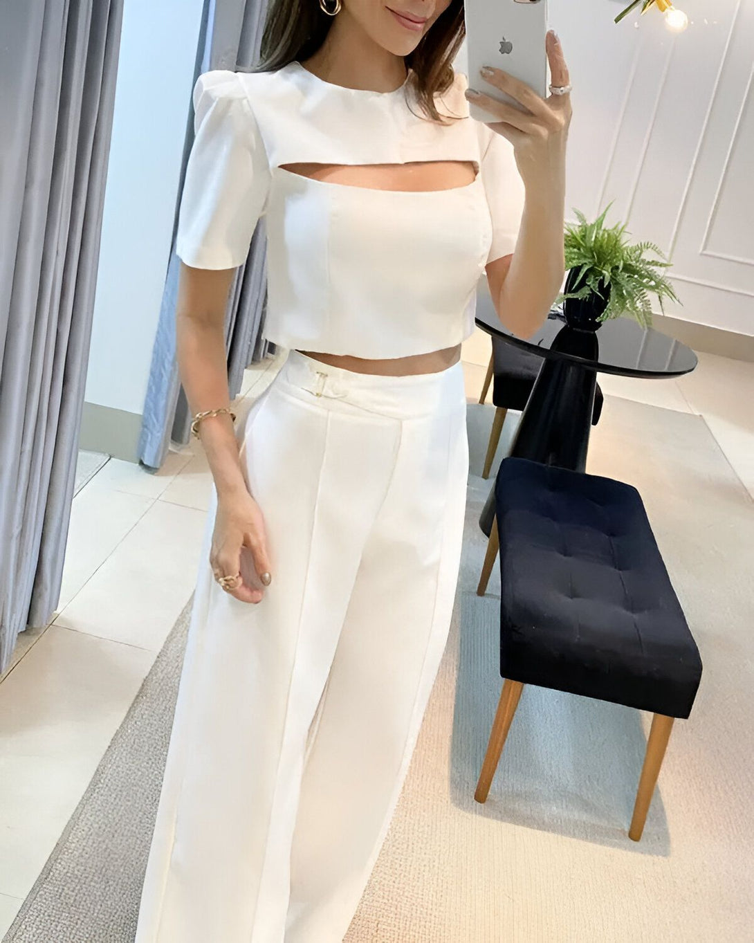 Une femme porte un ensemble pantalon et haut blanc. Le haut est court et possède des manches bouffantes. Le pantalon est large et taille haute.