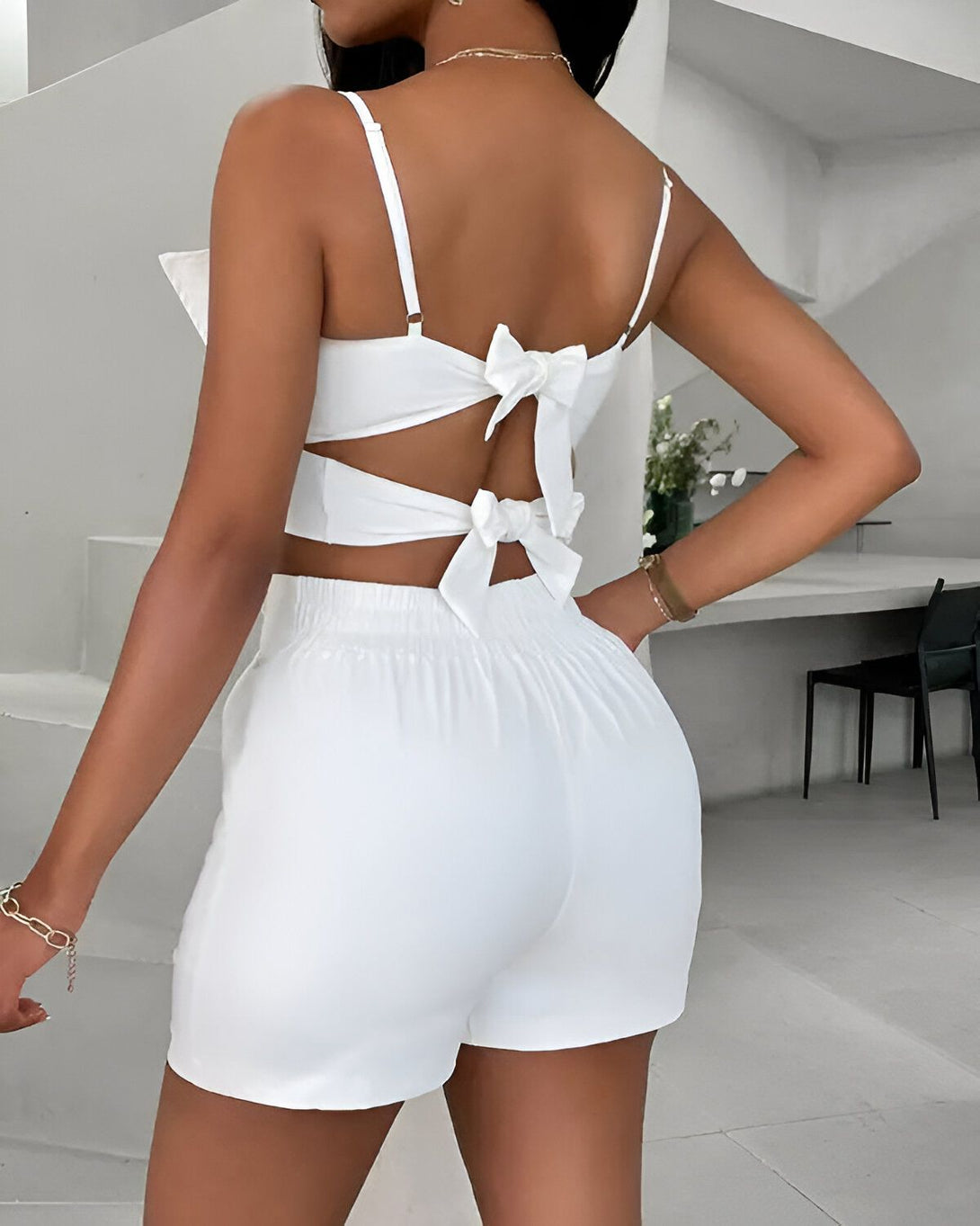 Une femme porte un ensemble short et haut blanc. Le haut est court et noué dans le dos. Le short est taille haute et évasé.
