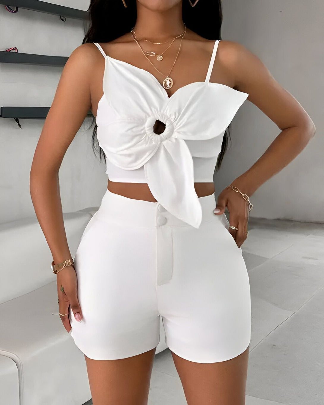 Une femme porte un ensemble deux pièces blanc composé d'un crop top et d'un short. Le crop top est noué sur le devant et le short est taille haute.