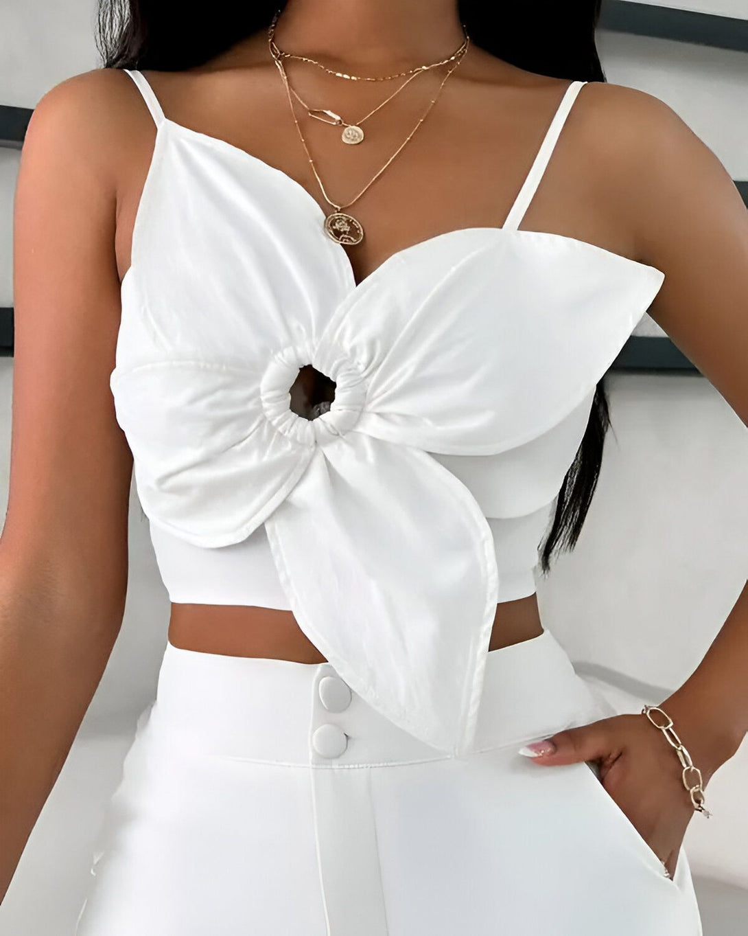 Une jeune femme porte un haut blanc court avec un détail de fleur sur le devant. Elle porte également un pantalon blanc taille haute et des talons blancs.