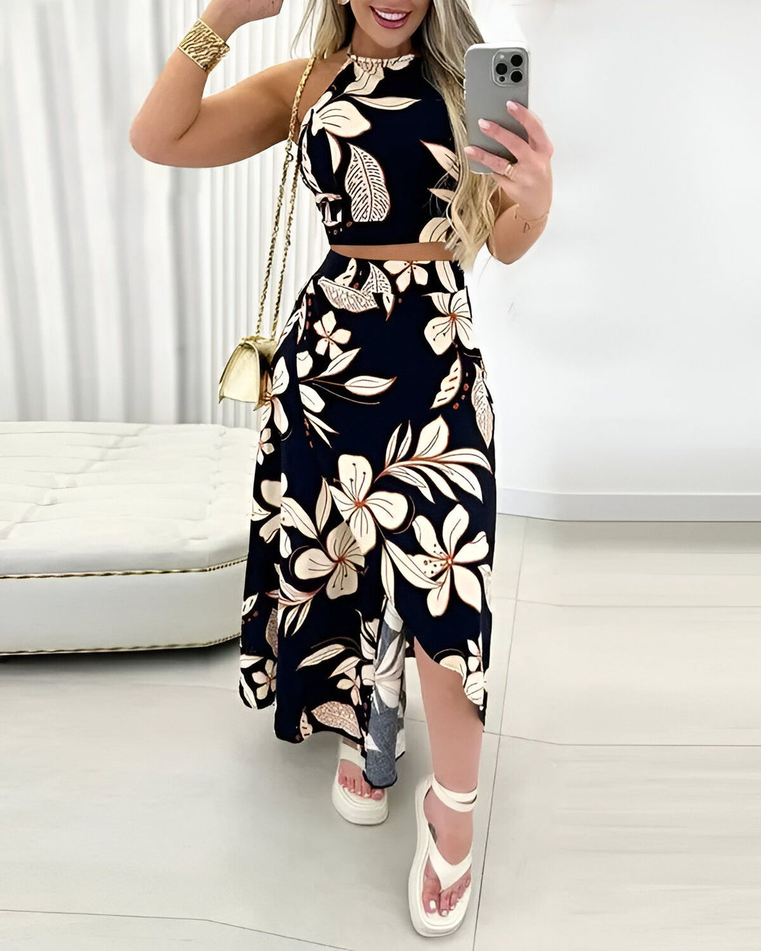 Une femme porte un ensemble deux pièces noir et blanc à motifs floraux. Le haut est un crop top à col montant et le bas est une jupe longue fendue sur le côté. Elle porte des sandales à talons blancs et un sac à main blanc.