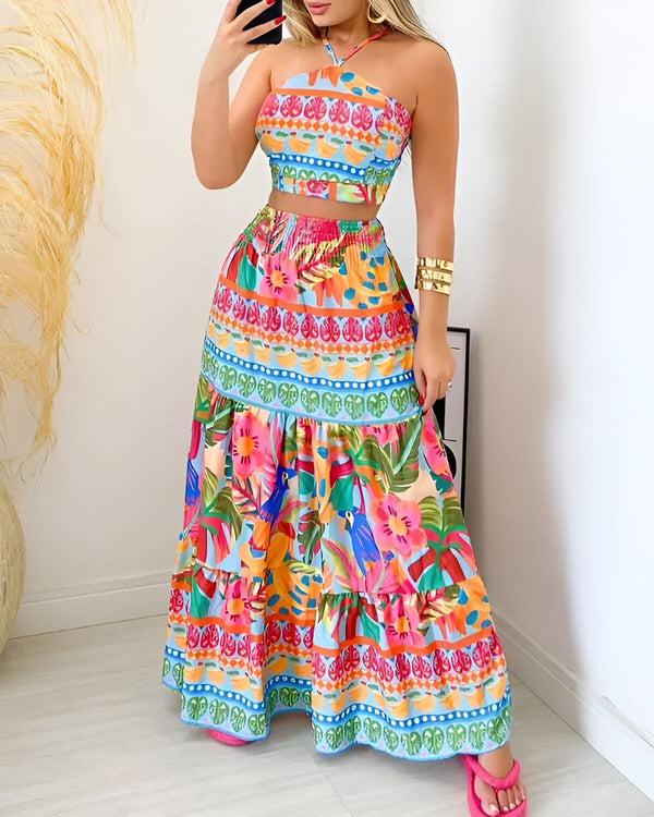 Une femme porte un ensemble deux pièces coloré avec un haut court et une jupe longue. Le haut est bleu clair avec un motif de feuilles tropicales et le bas est coloré avec un motif de fleurs et d'oiseaux.