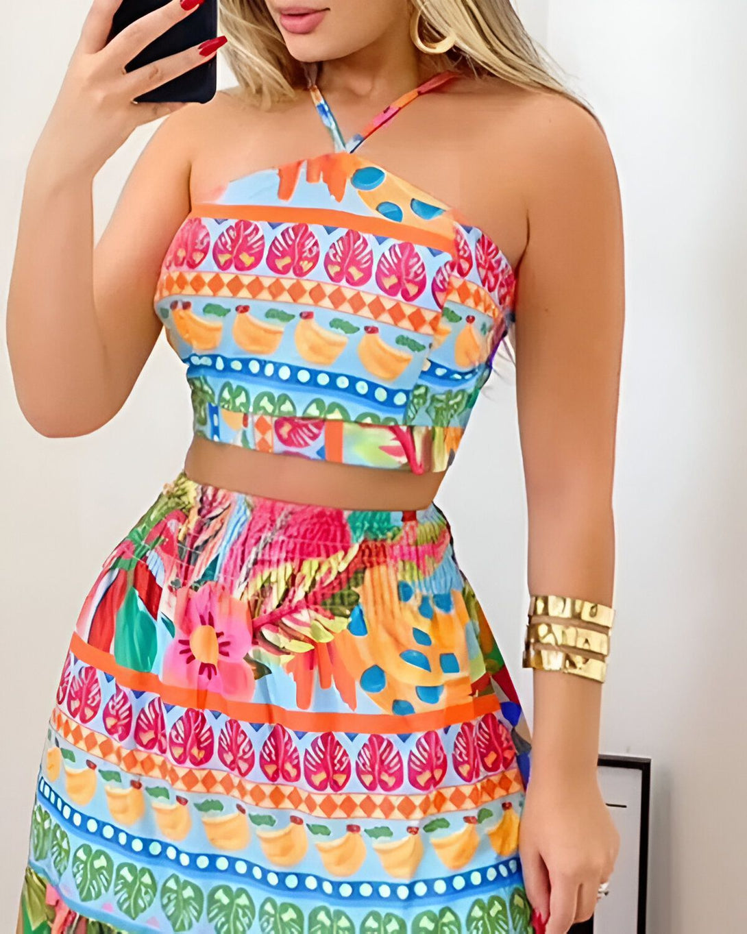 Une femme porte un ensemble coloré composé d'un crop top et d'une jupe courte. Le crop top est orange et bleu avec un motif de feuilles tropicales. La jupe est verte et orange avec un motif de fleurs tropicales.