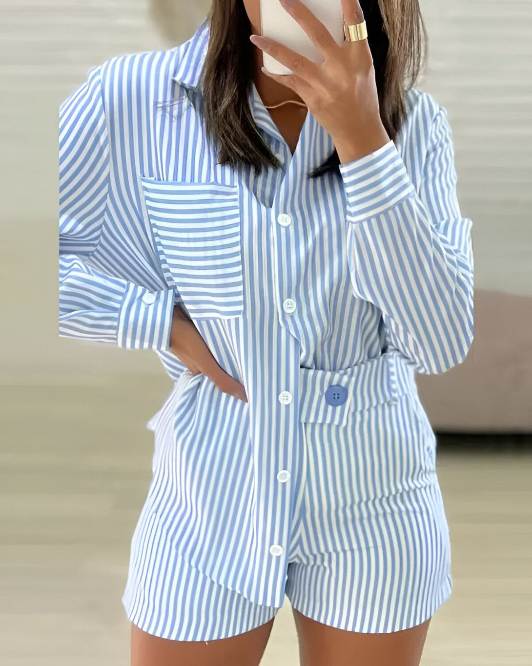 Une femme porte un ensemble de pyjama bleu et blanc à rayures verticales. Le haut est une chemise à manches longues avec un col et des boutons. Le bas est un short avec des poches.