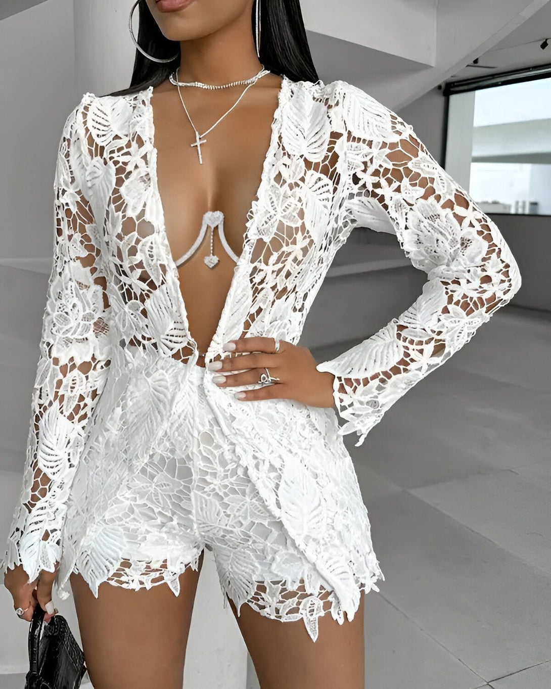 Une femme porte un ensemble short et veste en dentelle blanche. La veste est ouverte et laisse entrevoir un soutien-gorge blanc. La femme est également porte un collier avec un pendentif en forme de croix.