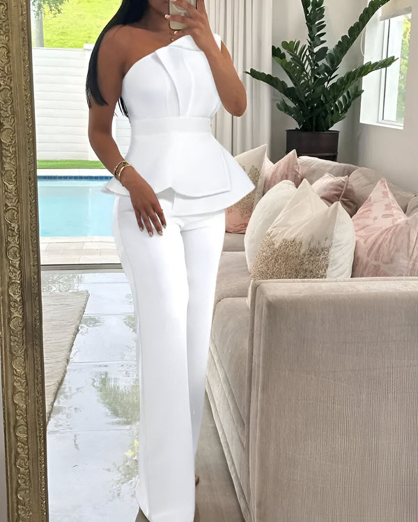 Une femme porte un pantalon et un haut blanc. Elle est debout dans un salon.