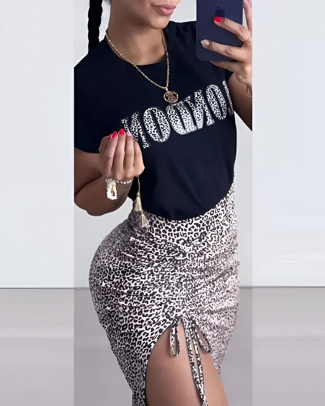Une femme porte un t-shirt noir avec le texte "Mourir" écrit en lettres blanches. Elle porte également une jupe léopard marron et noire.