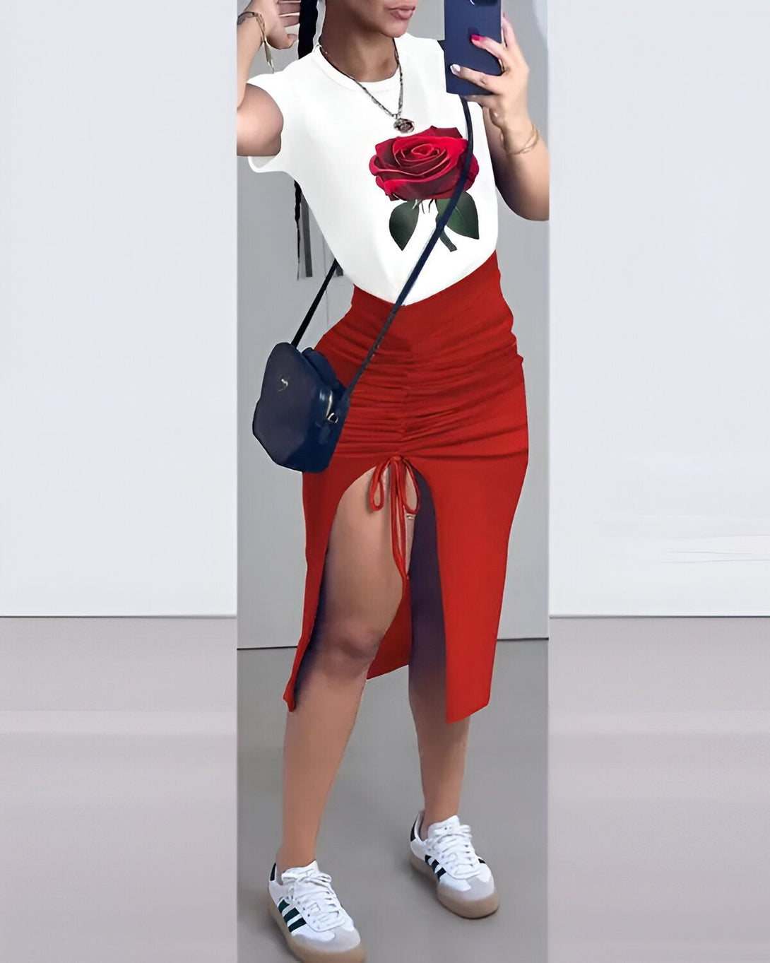 Une femme porte un t-shirt blanc avec une image d'une rose rouge. Elle porte également une jupe rouge fendue sur le côté. Elle porte des baskets blanches et un sac à main noir.