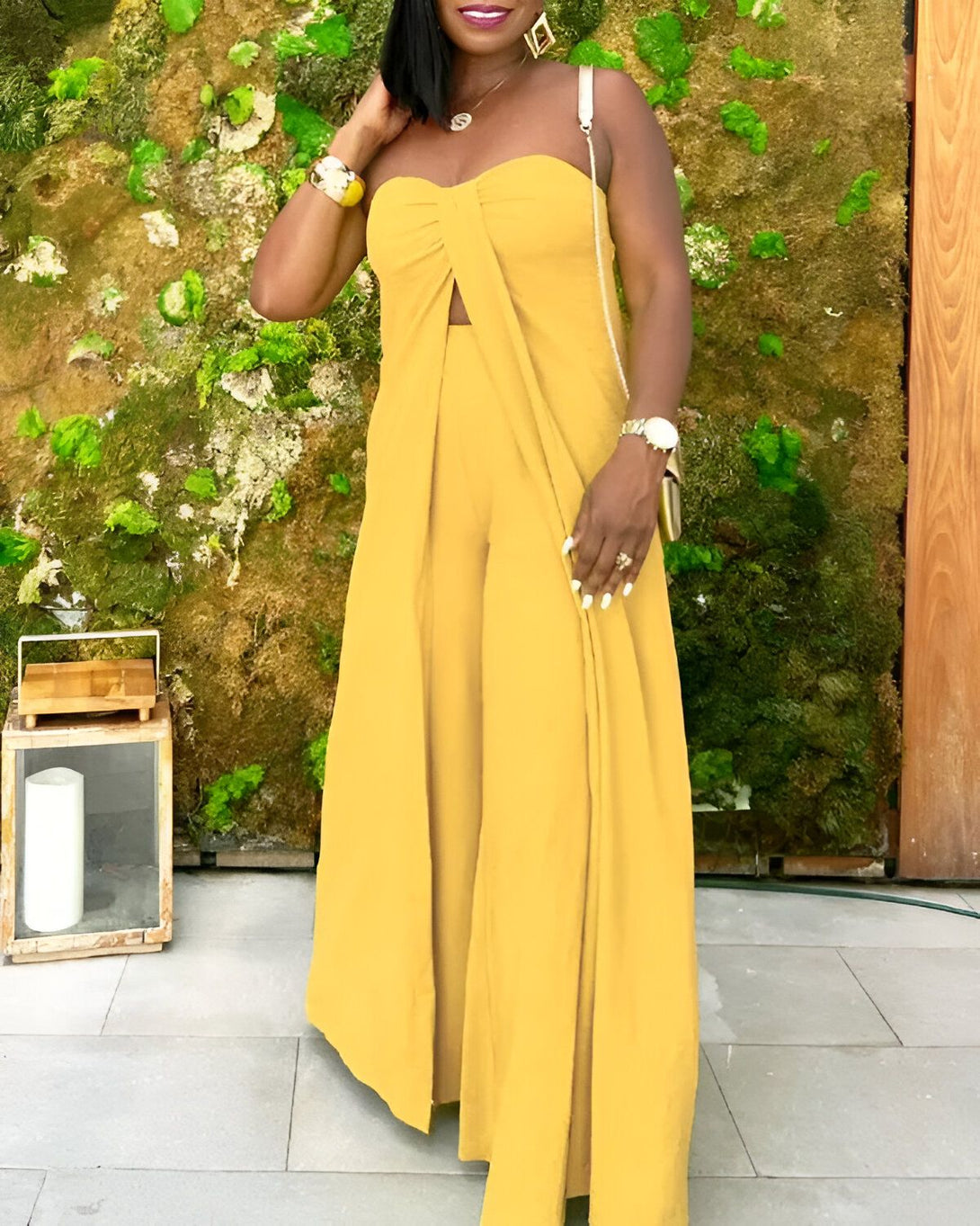 Une femme porte une combinaison pantalon jaune composée d'un haut bandeau et d'un pantalon large. Elle est accessoirisée d'un collier, de bracelets et d'une montre.