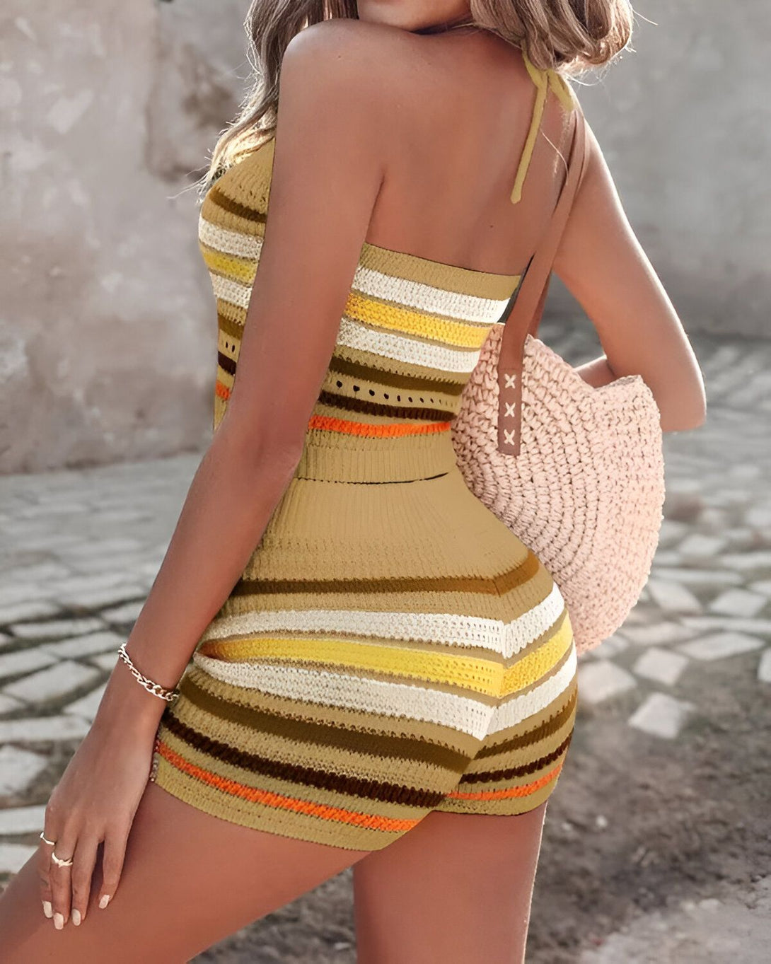 Une femme porte un haut court marron et blanc à rayures et un short marron et blanc à rayures. Elle porte également un sac à main beige et des sandales marron clair.