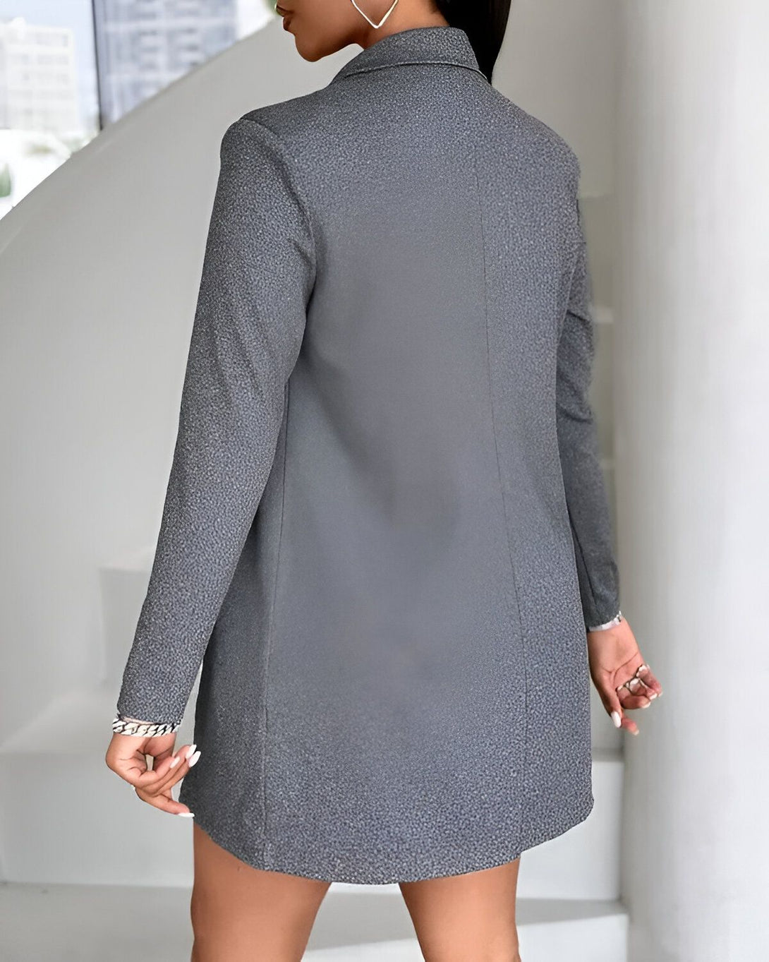 Une femme porte une veste de tailleur gris cintré avec des boutons argentés.