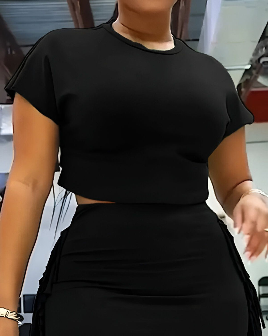 Une femme porte un ensemble deux pièces noir moulant avec des détails frangés sur les côtés.