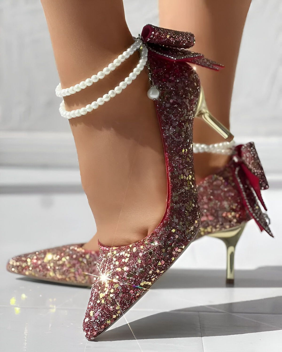Une image d'une paire d'escarpins à talons hauts rouges pailletés avec un nœud sur le devant et une bride perlée autour de la cheville.