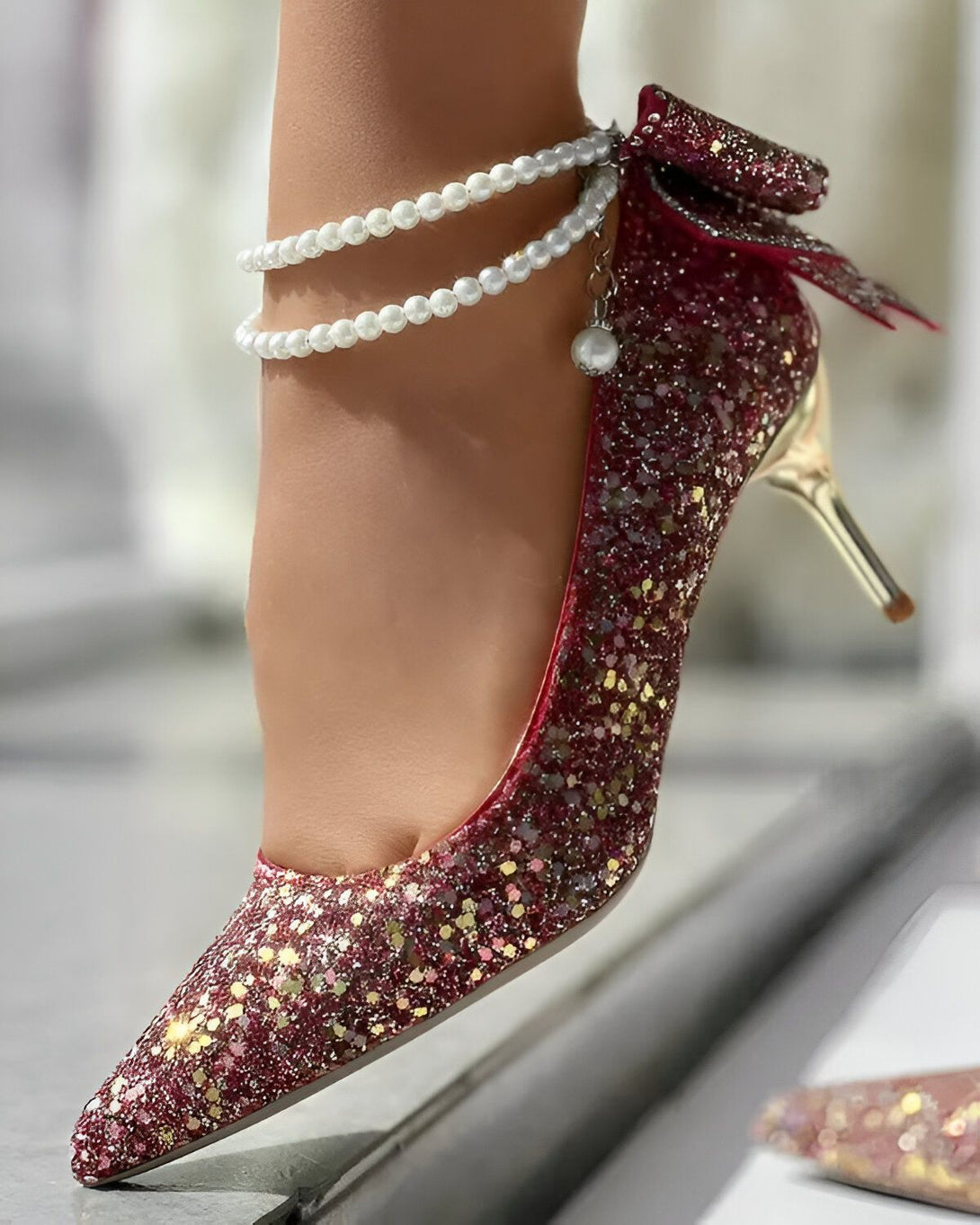 Une image d'une chaussure à talon rouge pailletée avec un nœud sur le devant et une bride perlée autour de la cheville.