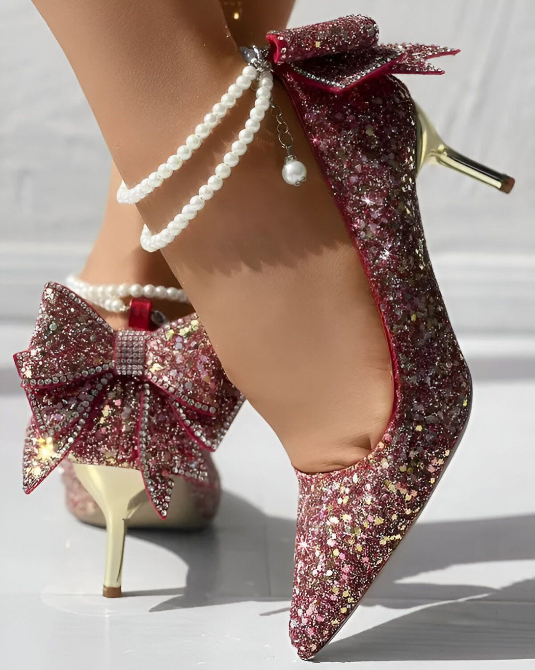 Une image d'une paire d'escarpins à talons hauts roses pailletés avec un nœud en strass sur le devant et une bride cheville avec des perles.