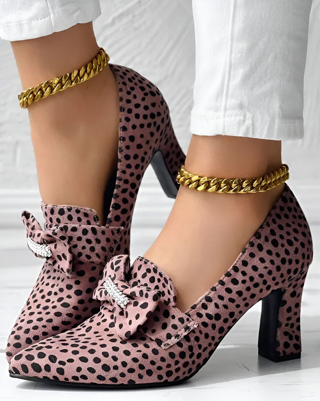 Une paire d'escarpins roses à talons hauts avec un nœud sur le devant et une chaîne dorée autour de la cheville.