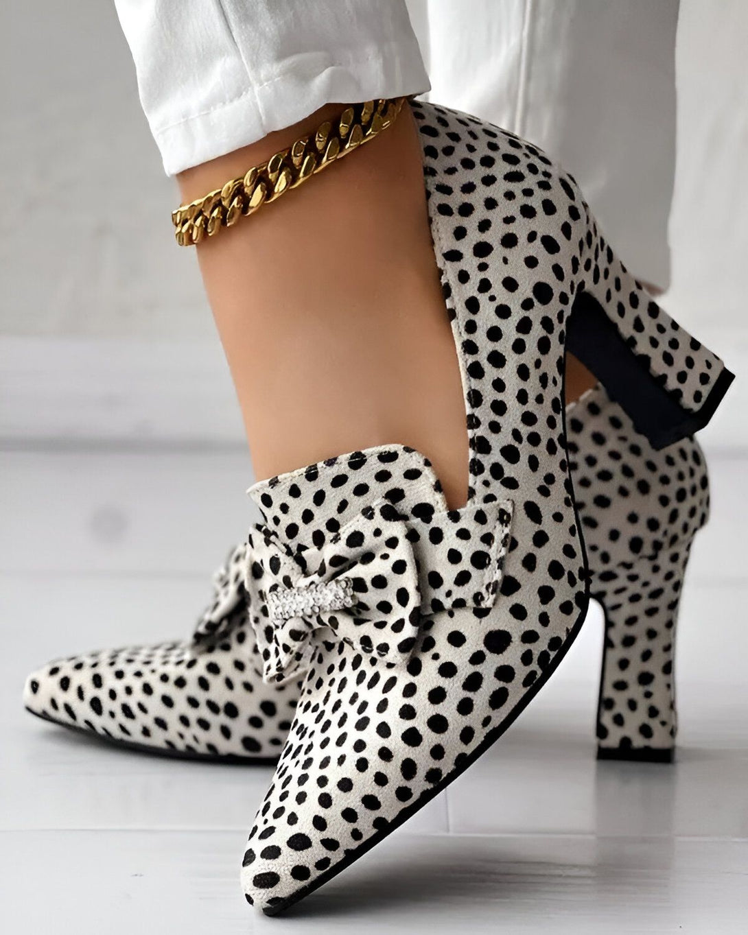 Une image d'une paire d'escarpins à talons hauts noirs et blancs à pois avec un nœud décoratif sur le devant. Les chaussures sont portées par une femme qui porte un pantalon blanc et un chemisier noir.