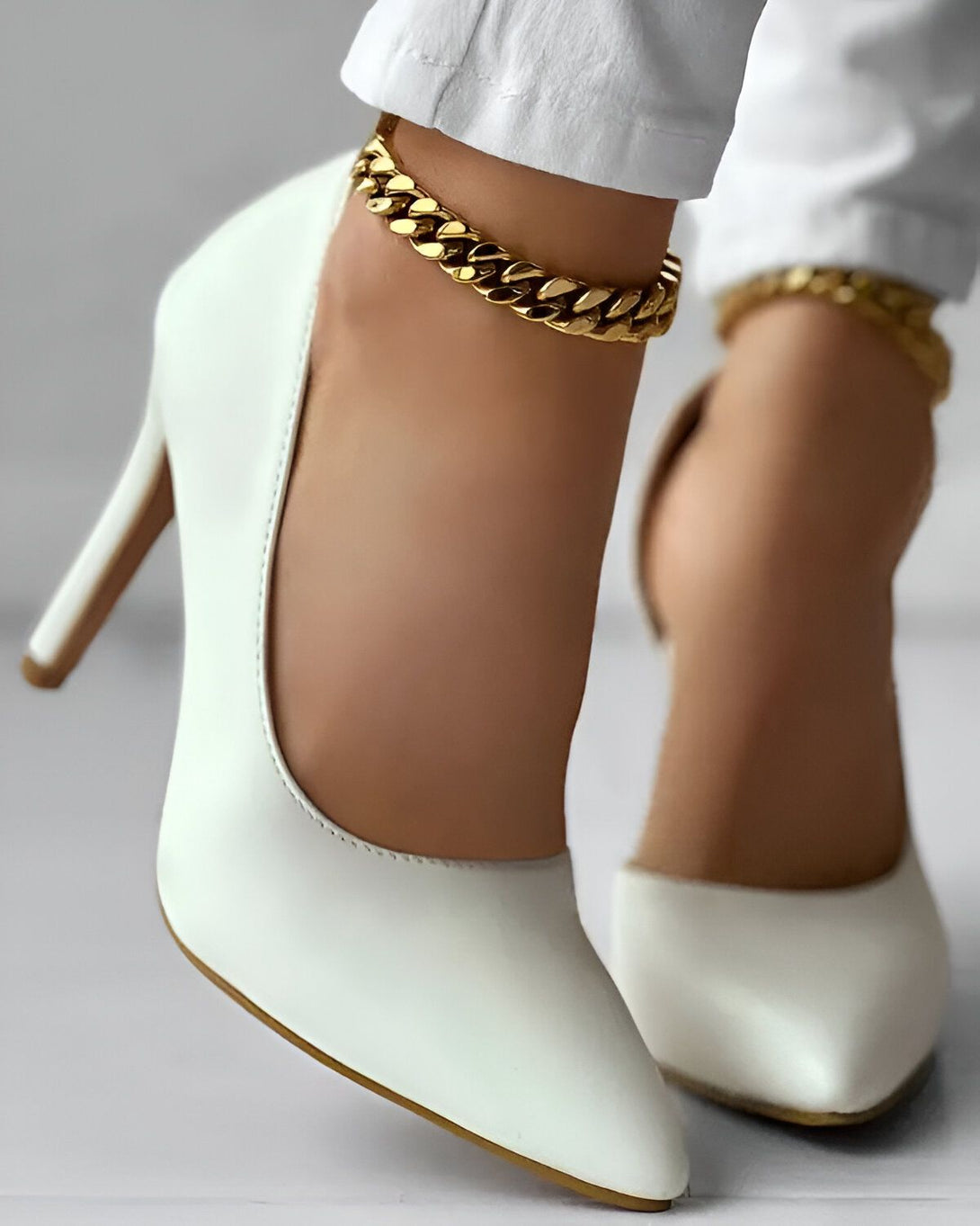 Une image d'une femme portant des escarpins blancs à talons hauts et un bracelet de cheville en or.