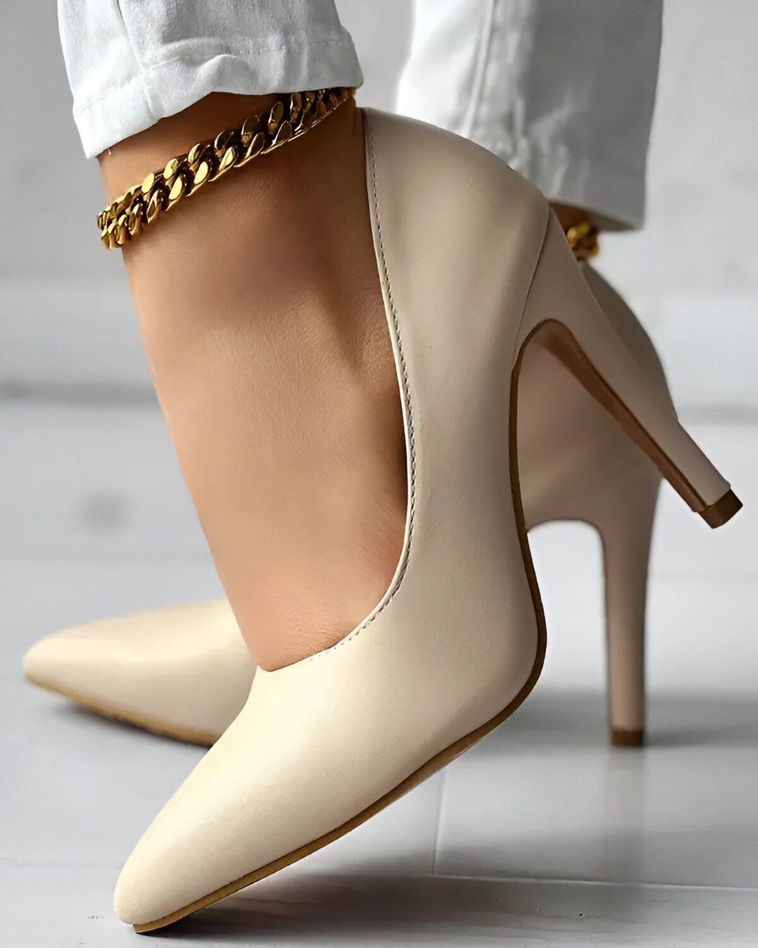 Une femme porte des escarpins blancs à talons hauts. Elle porte également un bracelet de cheville en or.