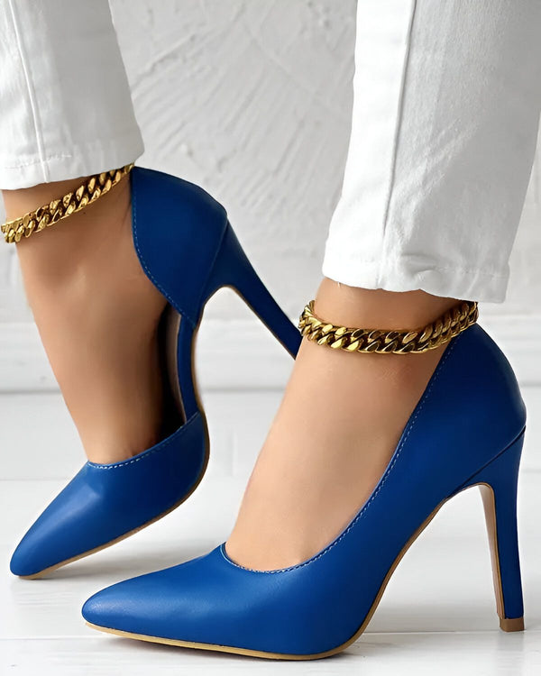 Une femme porte des escarpins bleus à talons hauts. Les chaussures ont une chaîne dorée autour de la cheville. La femme porte un jean blanc et les escarpins sont de couleur bleu roi.